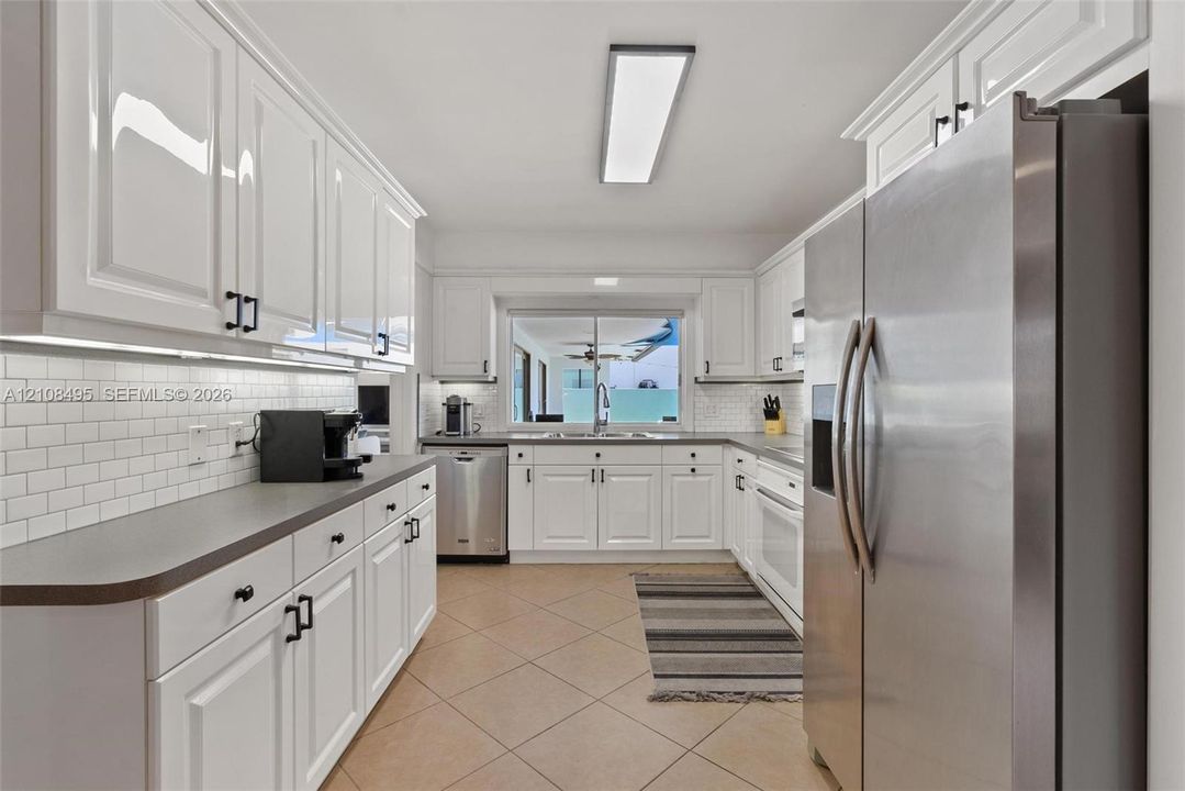 Kitchen featuring white shaker-style cabinetry, matte black hardware, white subway tile backsplash, solid-surface countertops, and stainless steel appliances