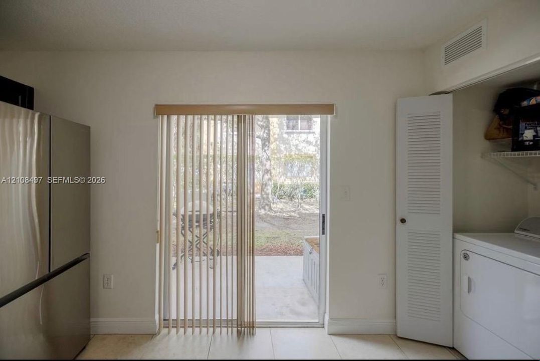 Sliding glass door with vertical blinds, stainless steel refrigerator, louvered closet door, and tile flooring