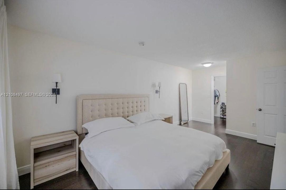 Bedroom interior featuring dark wood-finish flooring, recessed ceiling lighting, wall-mounted light fixtures, and a white six-panel interior door