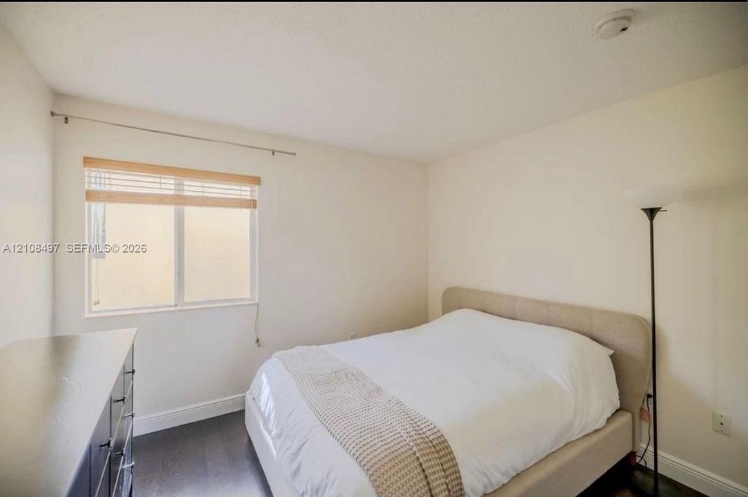 Room featuring dark wood-finish flooring, neutral wall tones, and a single-pane sliding window with horizontal slat blinds