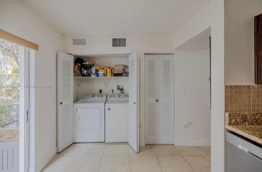 Laundry closet featuring side-by-side appliances, overhead shelving, and louvered folding doors, complemented by tile flooring and an additional louvered-door closet