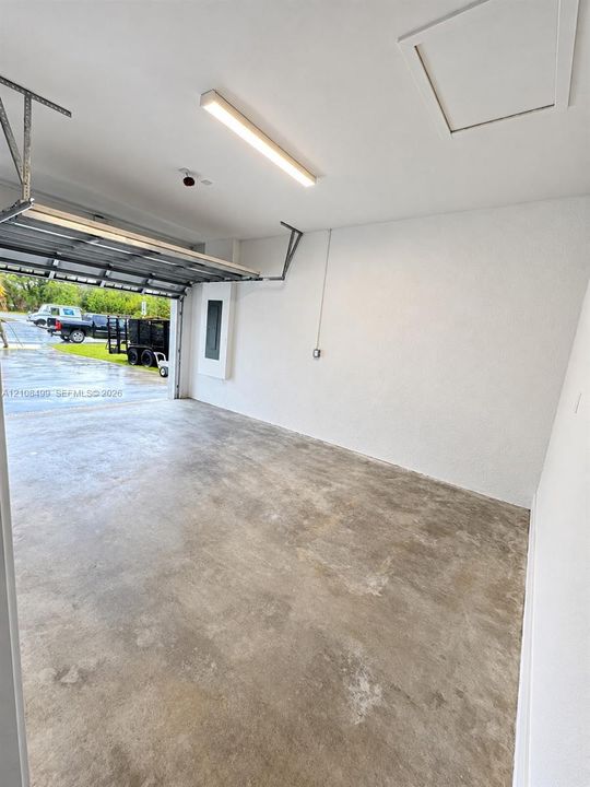 Finished garage featuring smooth-texture walls, a concrete floor, a linear LED light fixture, and an attic access panel