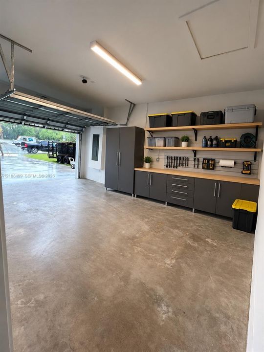 Garage featuring custom floor-to-ceiling cabinetry, integrated wall-mounted slat organization, wood-surfaced built-in workbench, and overhead linear lighting