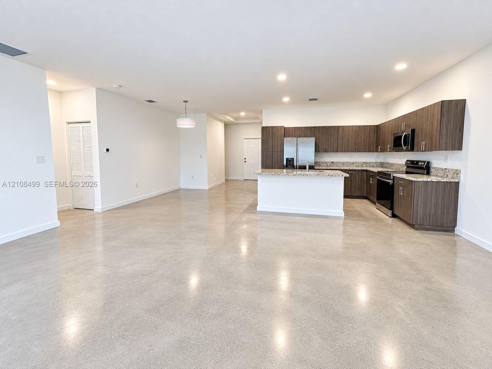 Polished concrete flooring, recessed lighting, horizontal wood-grain cabinetry, stone-surface countertops, and built-in stainless steel appliances