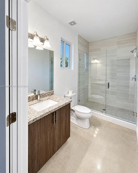 Bathroom featuring a wood-finish vanity with a stone countertop, an integrated rectangular sink, a glass-enclosed shower with tile surround, and polished concrete flooring