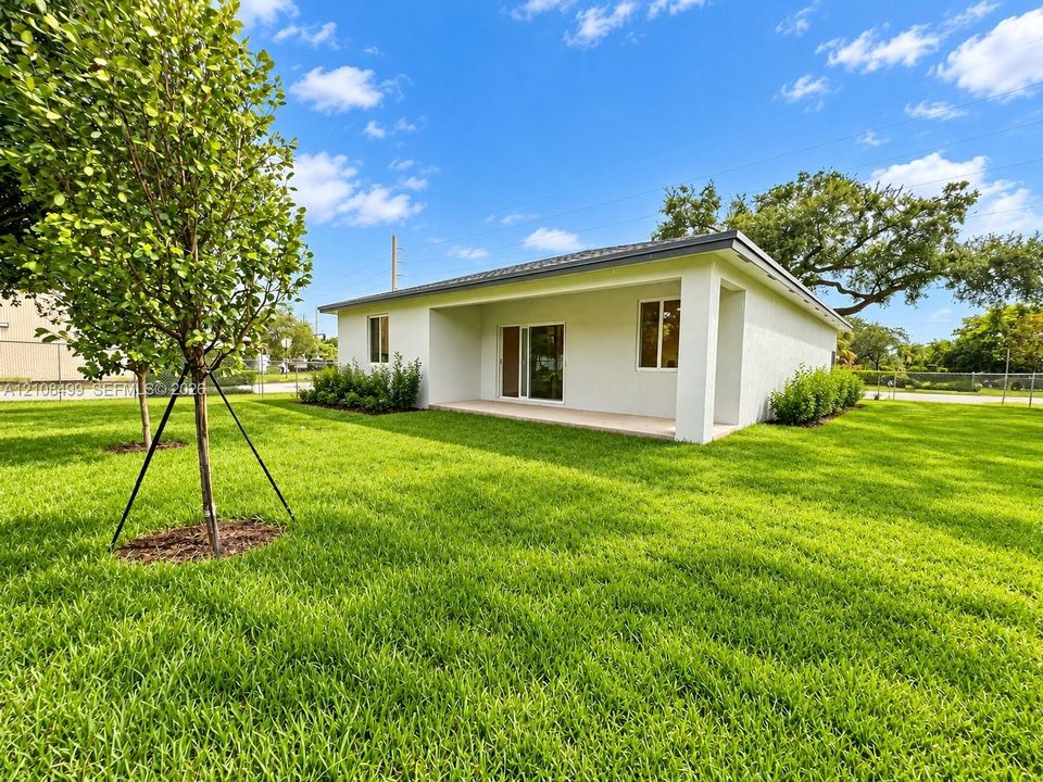 Stucco exterior featuring a covered patio, sliding glass door, and expansive grass lawn with mature trees