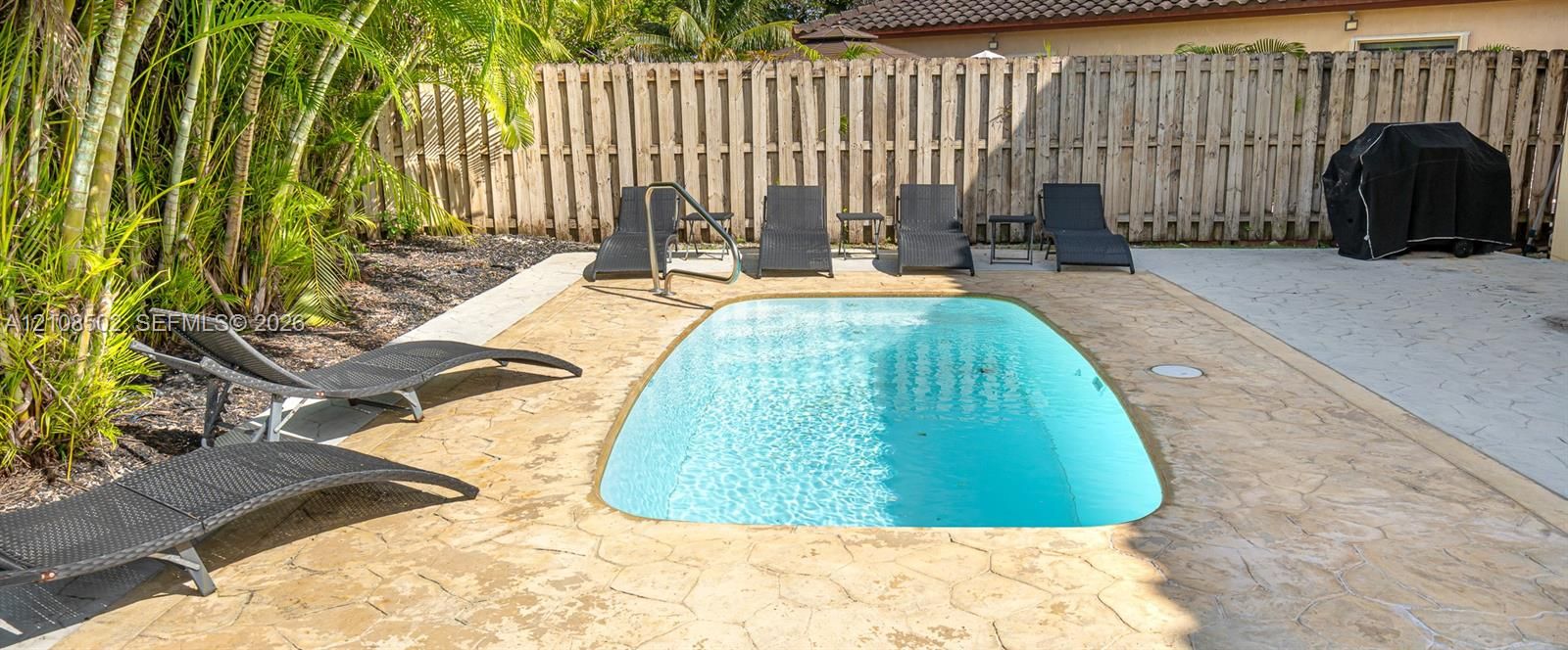 In-ground swimming pool with stamped concrete decking and privacy fencing
