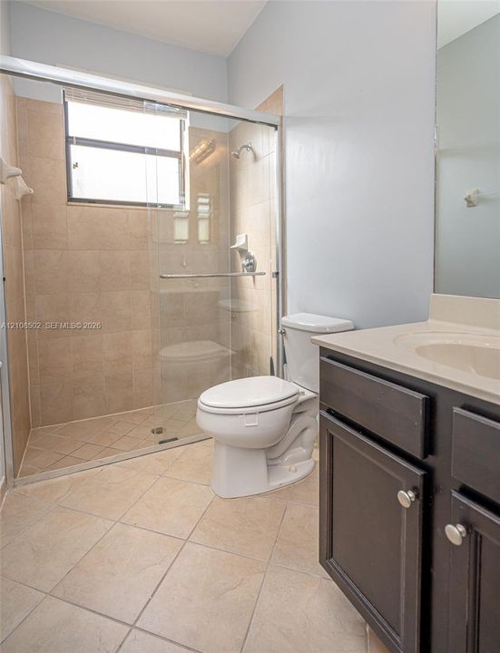 Bathroom featuring a glass-enclosed walk-in shower with tile surround, dark wood-finish cabinetry, and a solid-surface vanity countertop