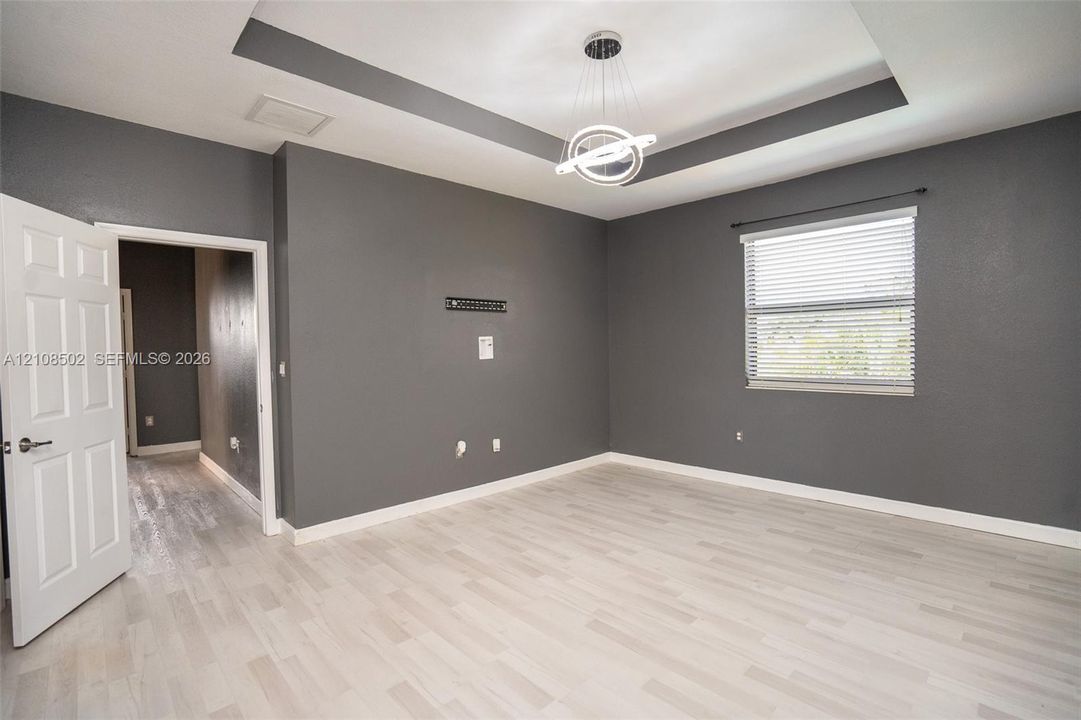 Tray ceiling with integrated lighting, wood-finish flooring, and contemporary circular pendant fixture
