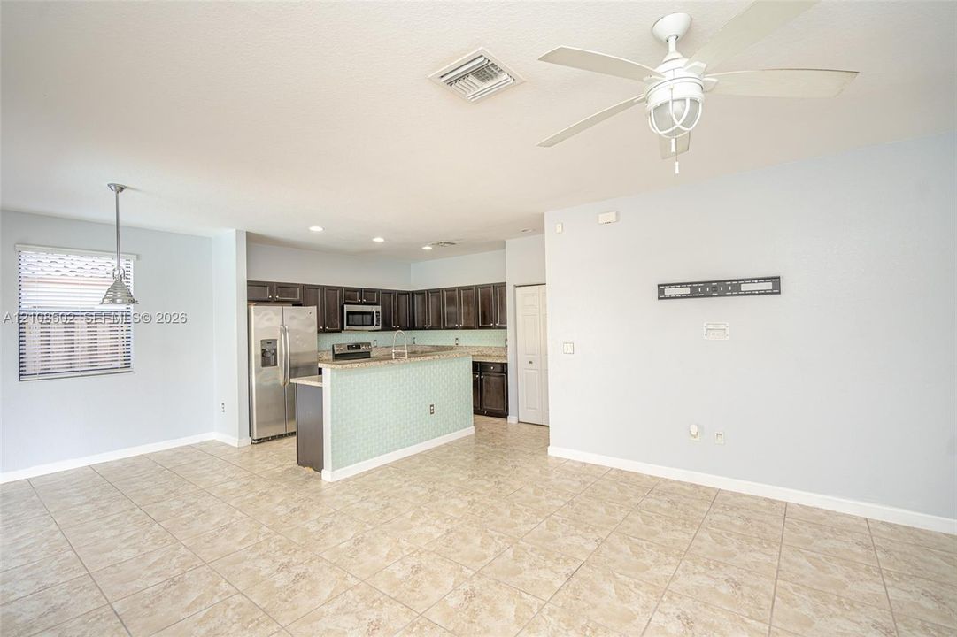 Open-concept floor plan featuring tile flooring, dark wood-finish cabinetry, stainless steel appliances, a peninsula counter, and a ceiling fan with integrated lighting