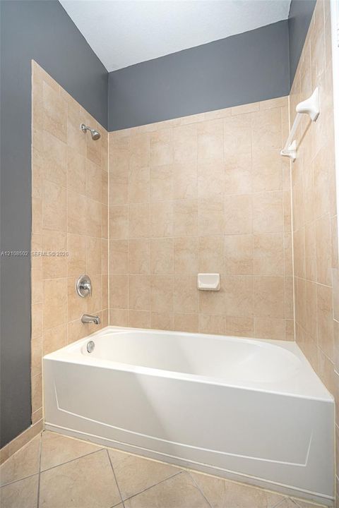 Bathtub with a shower head, tiled surround, built-in soap dish, and chrome fixtures