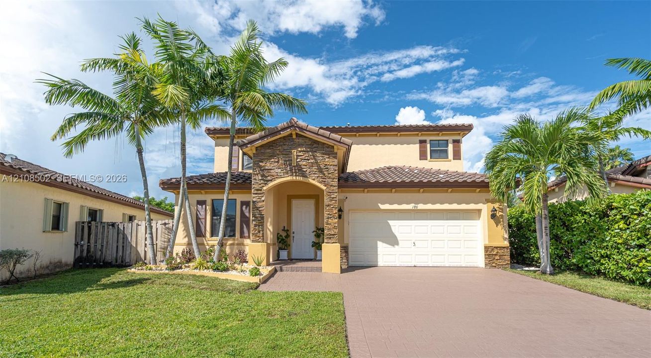 Two-story residence featuring a tile roof, stone-veneer entryway, stucco exterior, attached garage, and paved driveway