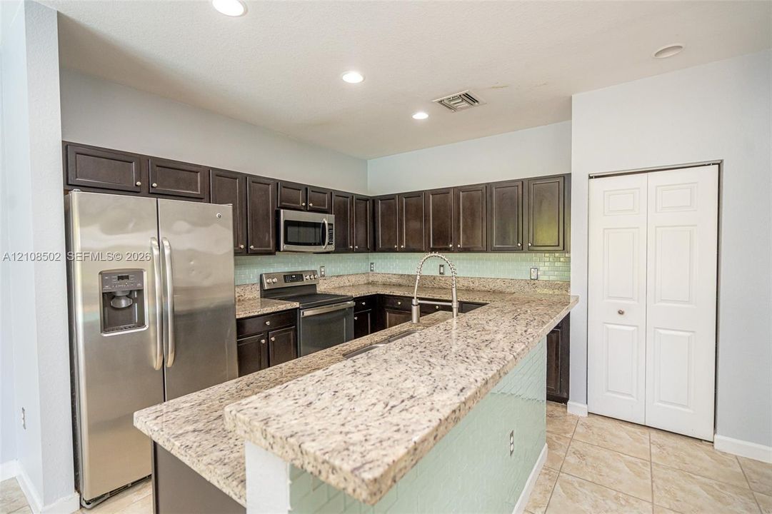 Kitchen featuring dark cabinetry, stone-finish countertops, subway tile backsplash, stainless steel appliances, and tile flooring