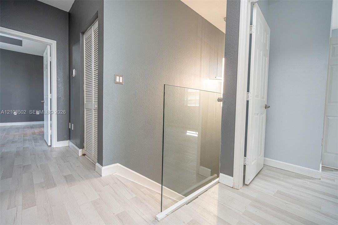 Tempered glass stair railing, light wood-finish flooring, and white paneled doors
