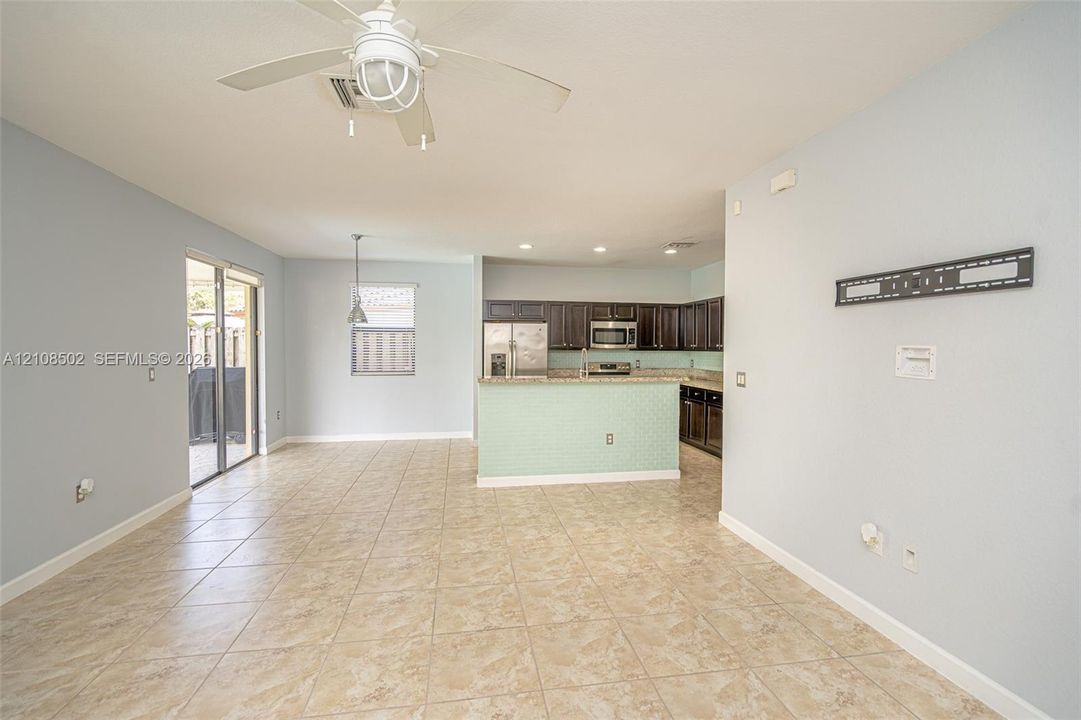 Open-concept interior featuring tile flooring, a kitchen peninsula with a tiled front, dark-finish cabinetry, built-in stainless steel appliances, and a ceiling fan with integrated lighting