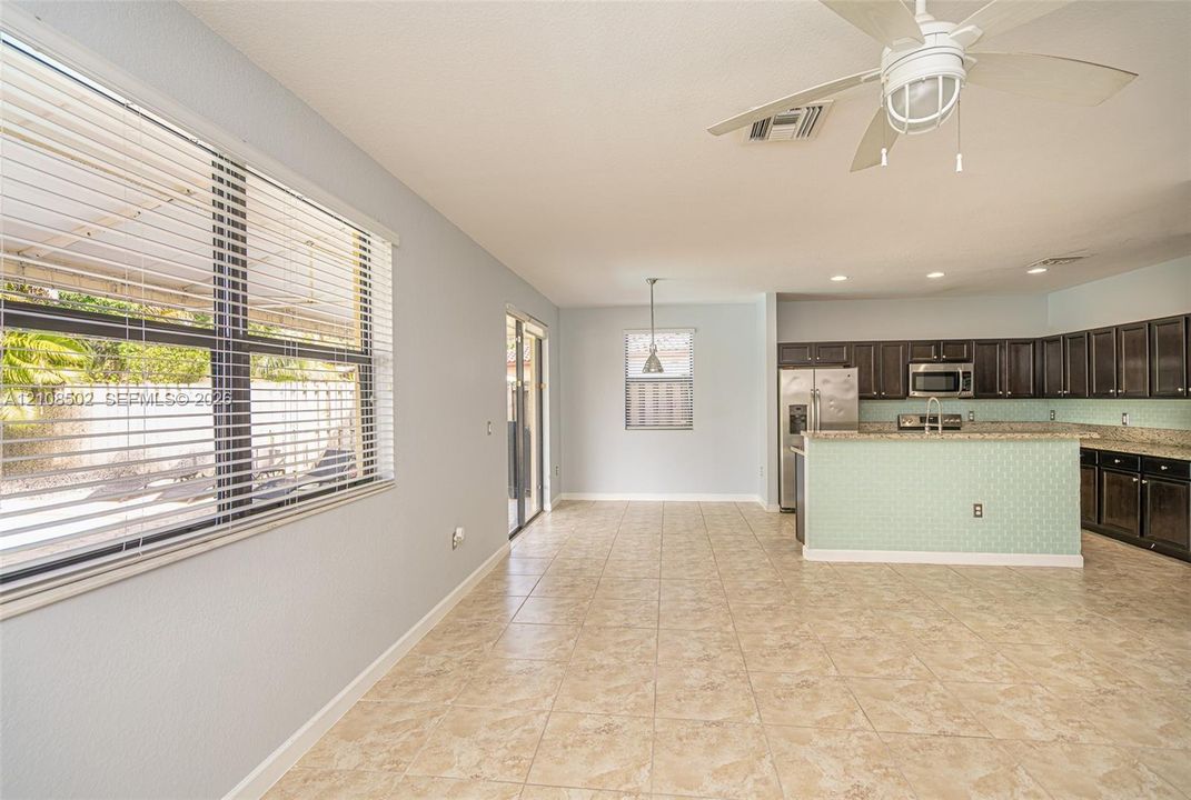 Open-concept area featuring tile flooring, a kitchen with dark cabinetry, stone-finish countertops, a tiled island facade, and a ceiling fan with integrated lighting
