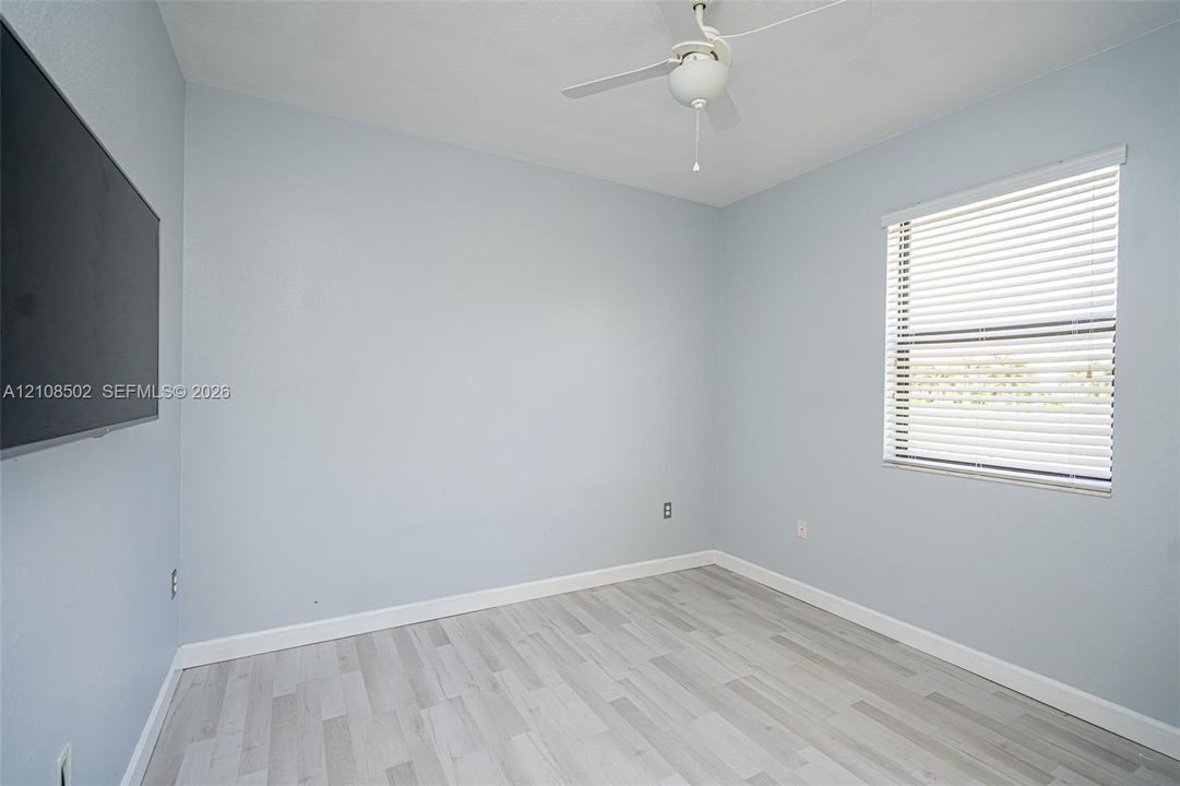 Neutral wall-toned room featuring wood-finish flooring, a white ceiling fan, and a window with horizontal blinds