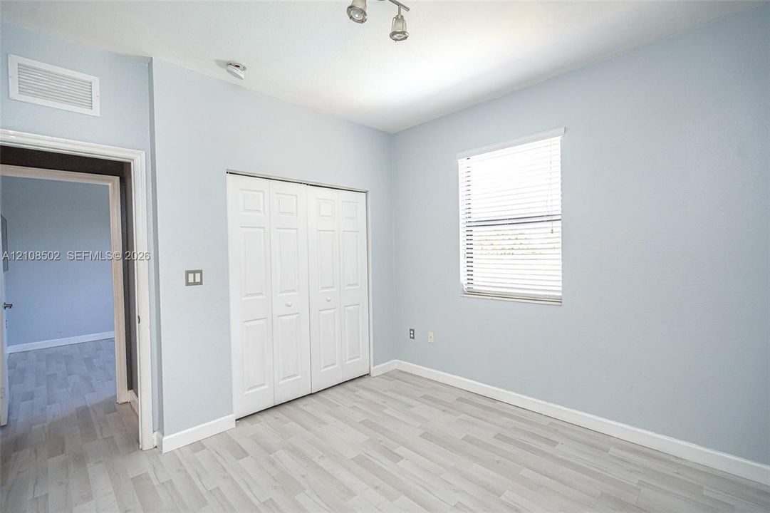 Room featuring wood-finish flooring, a double-panel closet with white doors, a single window with horizontal blinds, and a multi-bulb ceiling-mounted light fixture