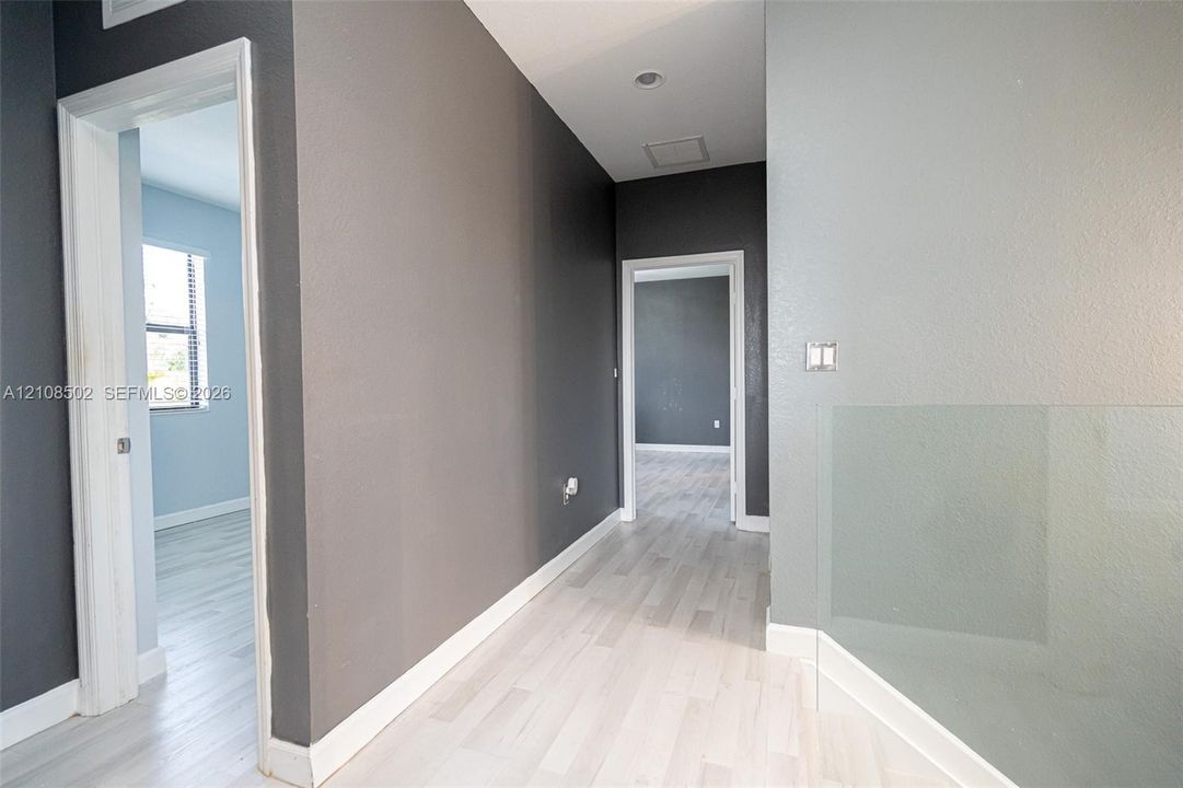 Interior hall featuring wood-finish flooring, two-toned wall paint, recessed lighting, and a minimalist glass panel railing