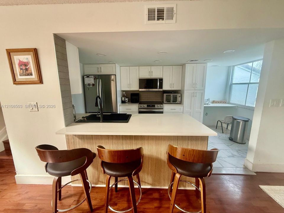Kitchen featuring white cabinetry, solid-surface countertops, integrated stainless steel appliances, a black undermount sink with a matte black faucet, and wood-finish cabinetry detailing