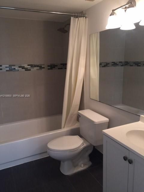 Bathroom featuring a bathtub with tile surround and decorative glass mosaic inlay, vanity with integrated basin, large wall-mounted mirror, and multi-bulb vanity lighting