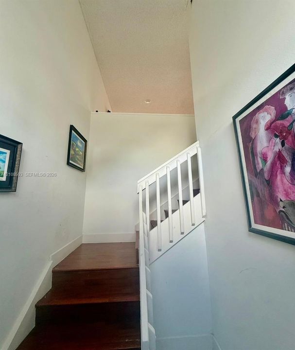 Staircase featuring wood-finish treads and a white wooden balustrade beneath a vaulted ceiling with recessed lighting