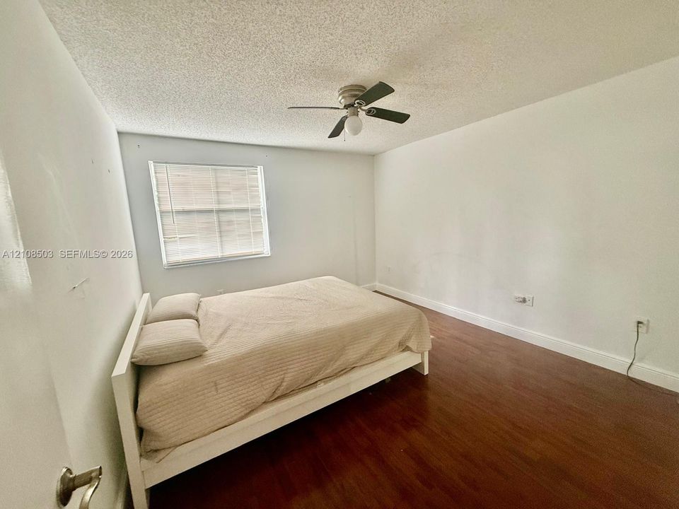 Room featuring wood-finish flooring, a ceiling fan with integrated lighting, and a window with horizontal blinds