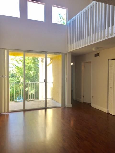 Double-height living area featuring wood-finish flooring, floor-to-ceiling sliding glass doors, upper-level interior balcony railing, and clerestory windows
