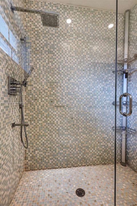 Walk-in shower featuring glass enclosure, mosaic tile wall surround, rainfall showerhead, handheld sprayer, and built-in corner shelving