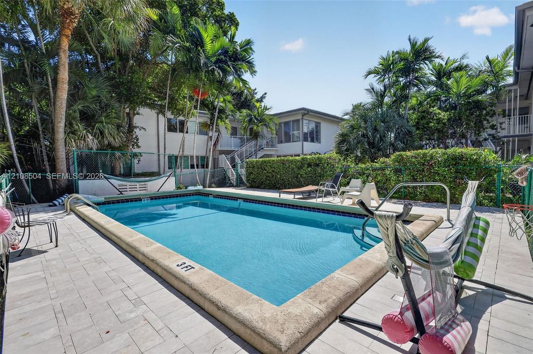 Swimming pool with concrete coping, surrounded by stone-paver decking, mature palm trees, and perimeter privacy hedging