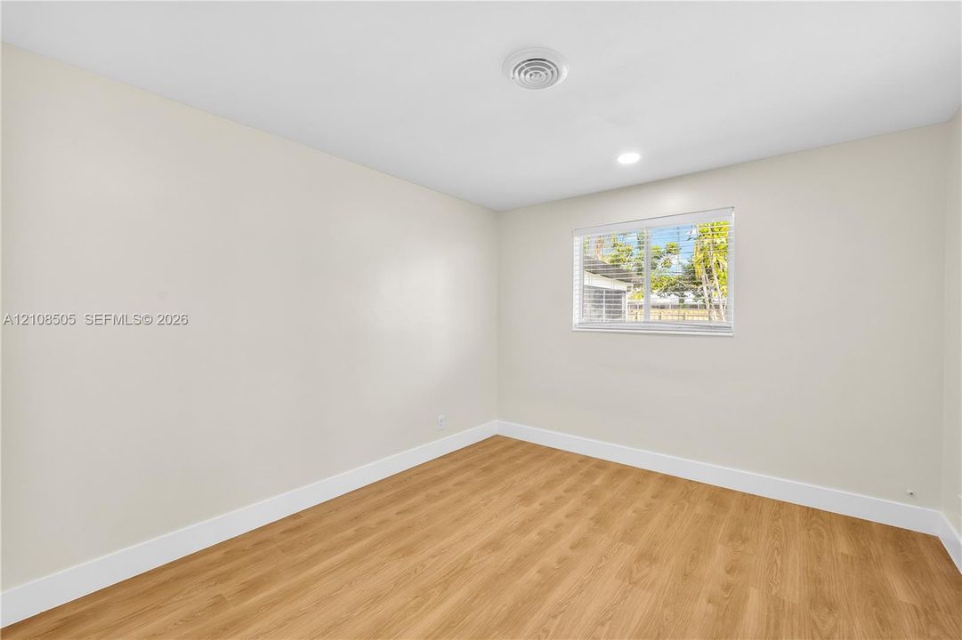 Neutral-toned interior space featuring wood-finish flooring and a single window with horizontal blinds