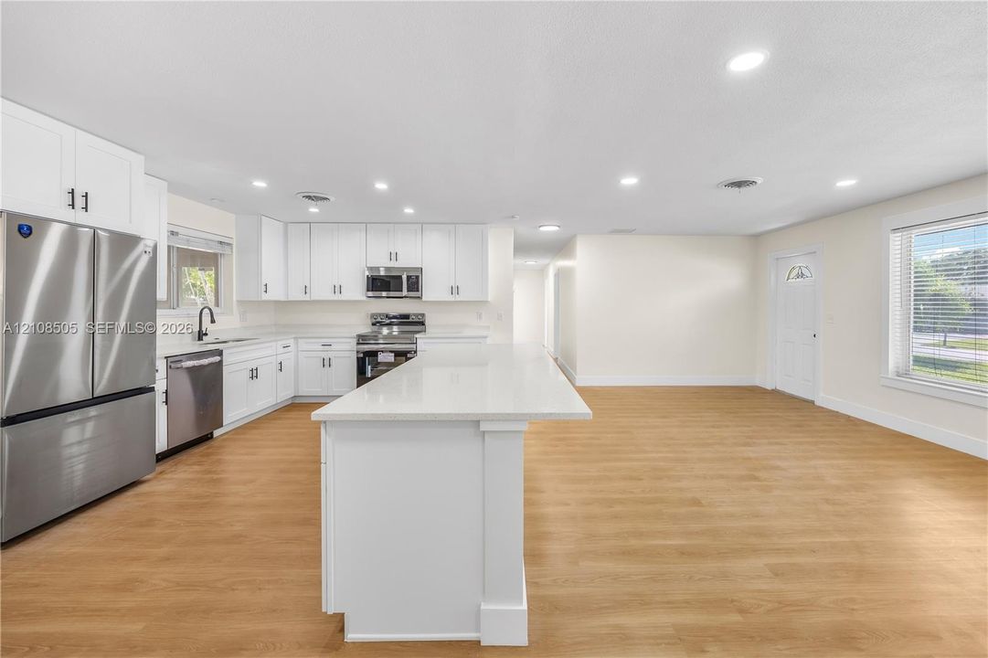 Kitchen featuring white cabinetry, an expansive central island with a solid-surface countertop, stainless steel appliances, and wood-finish flooring with recessed lighting