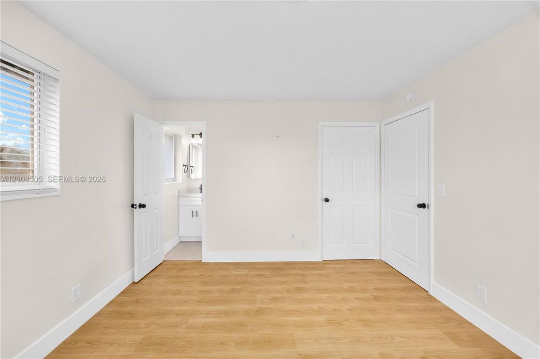 Room featuring wood-finish flooring, two white panel doors, and window with horizontal blinds