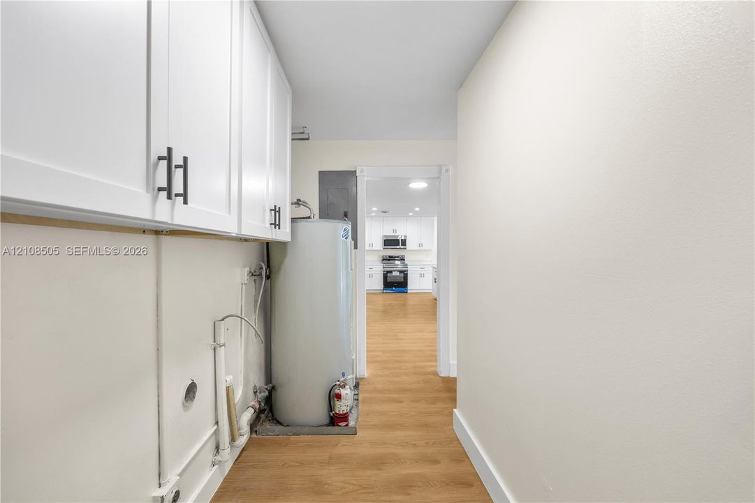 White cabinetry with matte black hardware, wood-finish flooring, and a water heater