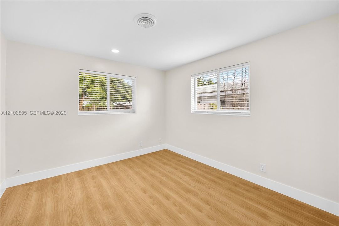 Neutral interior space featuring wood-finish flooring, dual windows with horizontal blinds, and recessed ceiling lighting