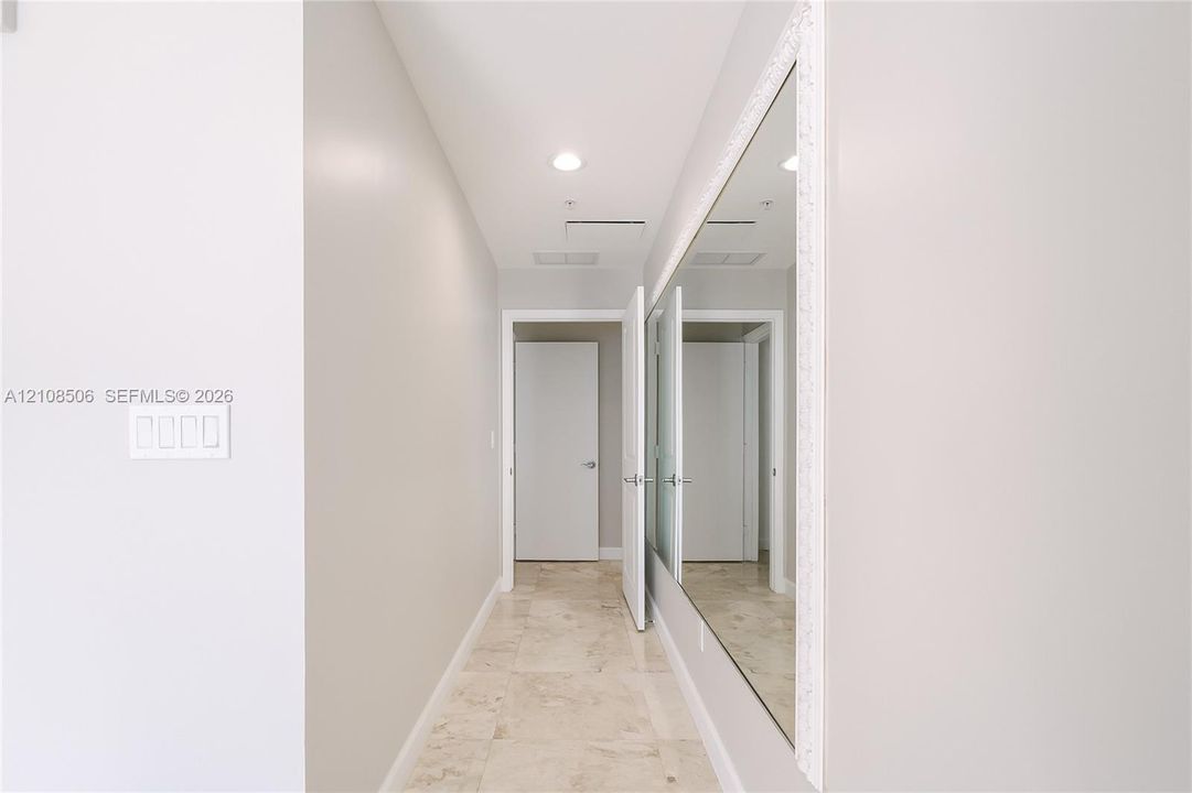 Hallway featuring stone tile flooring, recessed ceiling lighting, and an expansive wall-mounted mirror