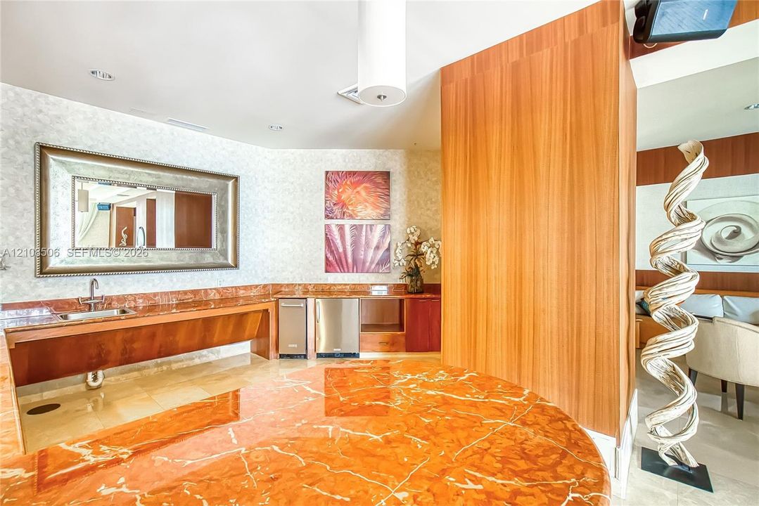 Custom vanity featuring a polished stone countertop with an integrated basin, stainless steel under-counter appliances, vertical wood-panel wall feature, and framed wall mirror