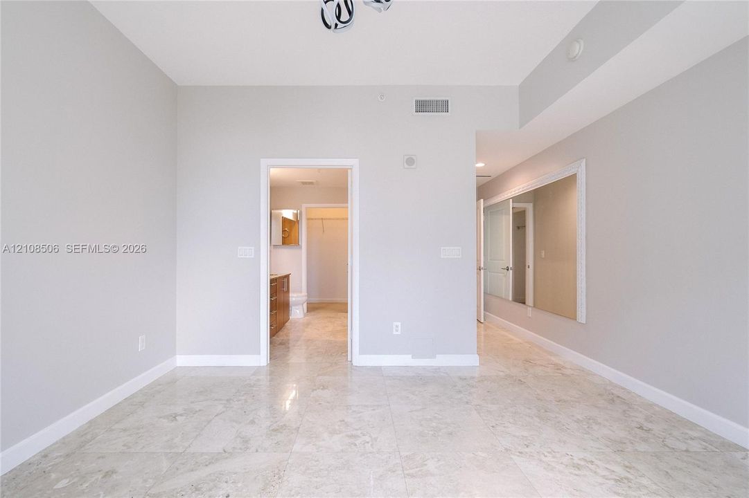 Interior room featuring neutral-toned stone-finish flooring, a large wall-mounted mirror, and a geometric flush-mount light fixture