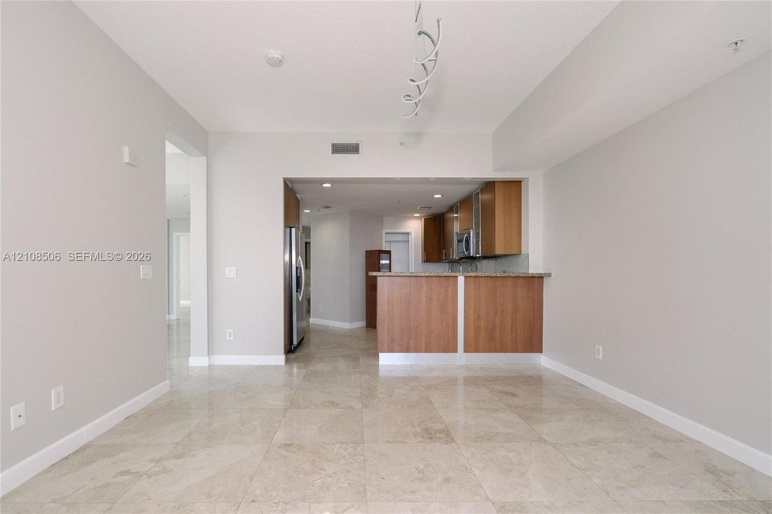 Open concept floor plan featuring light-toned tile flooring, wood-finish cabinetry, a peninsula breakfast bar, and stainless steel appliances