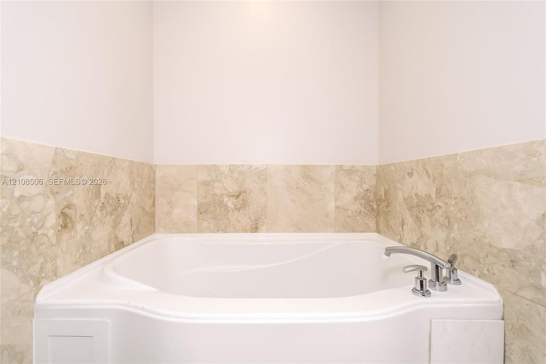 Built-in soaking tub with a polished chrome deck-mounted faucet, surrounded by neutral-toned stone tile wainscoting