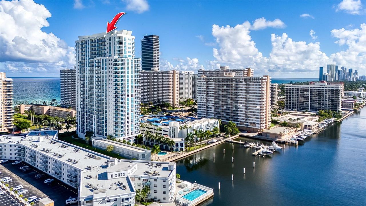 High-rise residential tower featuring multiple private balconies, floor-to-ceiling glass paneling, and an expansive concrete structure situated along the waterfront