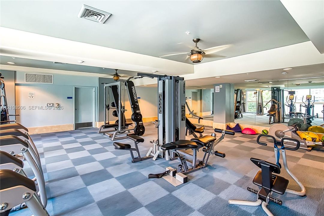 Multi-purpose room featuring a dual-toned checkerboard tile floor, mirrored wall accents, tray ceiling, and dual integrated ceiling fans