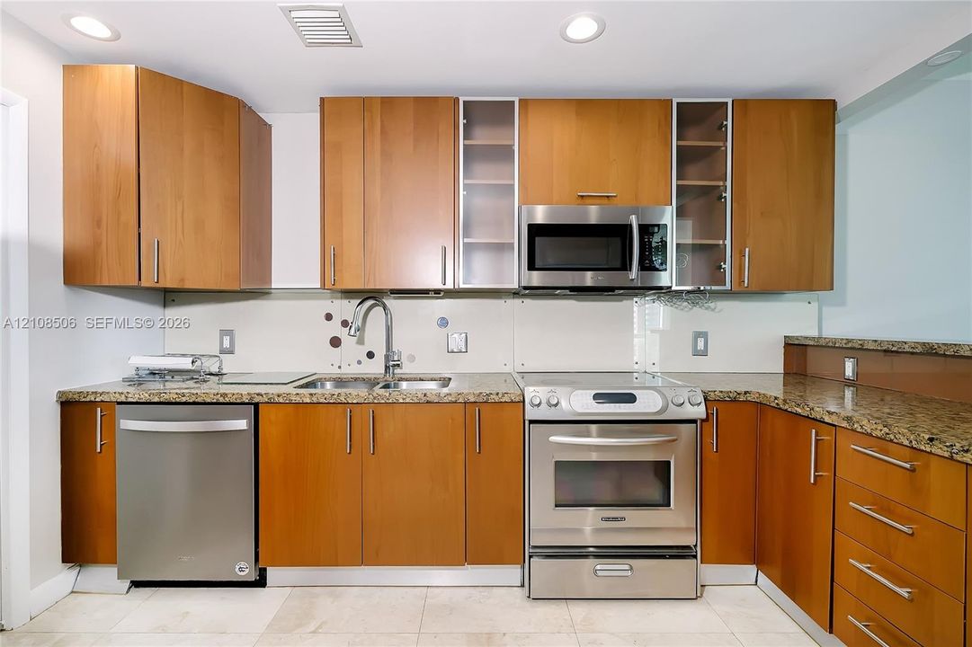 Kitchen featuring wood-finish cabinetry, stone-surface countertops, stainless steel appliances, glass-front upper cabinet doors, and recessed ceiling lighting