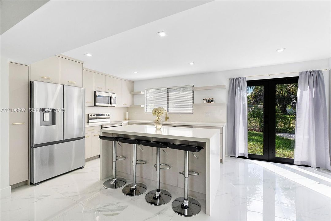 Kitchen featuring a center island with quartz countertop, stainless steel appliances, flat-panel cabinetry, recessed lighting, and large glass-panel doors