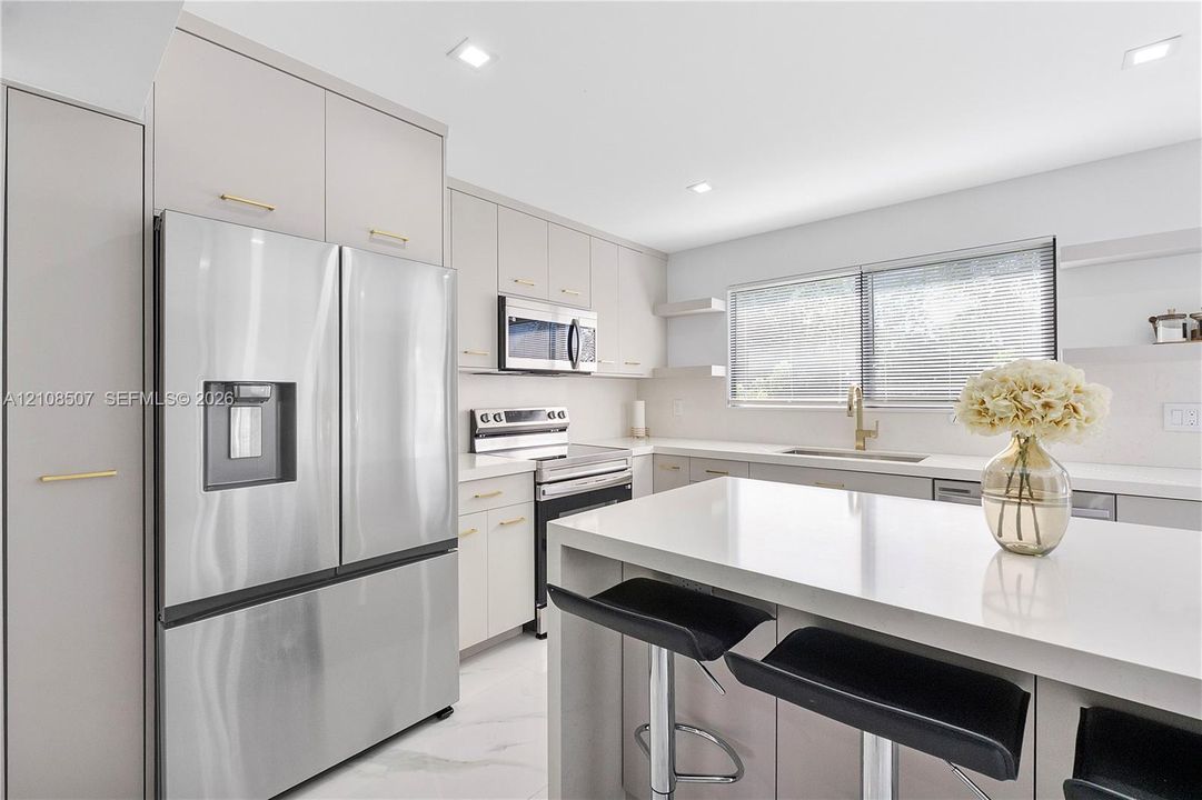Kitchen featuring flat-panel cabinetry with gold-tone hardware, a central island with a solid-surface countertop, stainless steel appliances, and recessed lighting