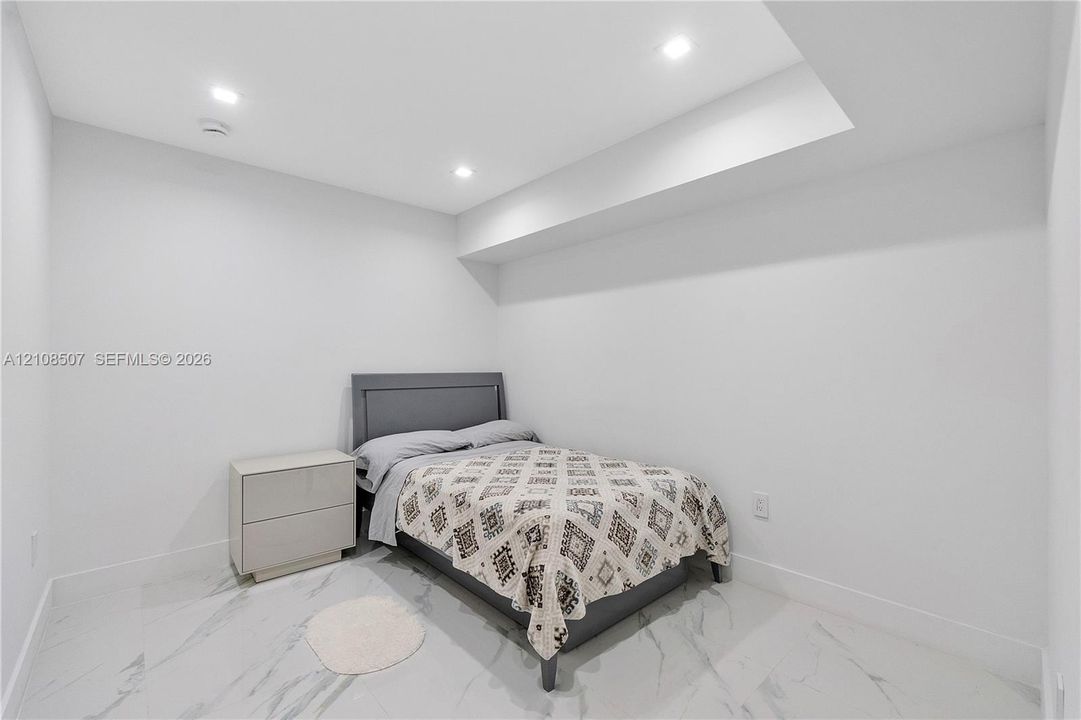 Neutral-toned interior space featuring light-colored stone-finish tile flooring, recessed ceiling lighting, and a recessed ceiling architectural detail