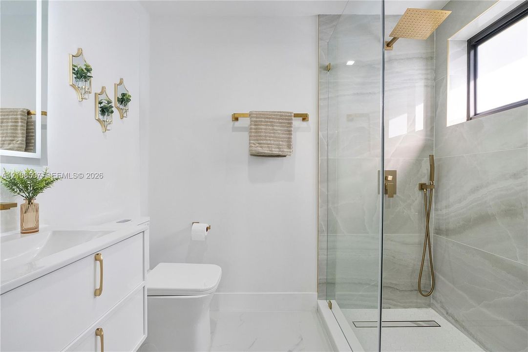 Floating vanity with integrated sink, brass hardware, walk-in shower with glass enclosure, wall-mounted rainfall showerhead, and tile-surround shower walls