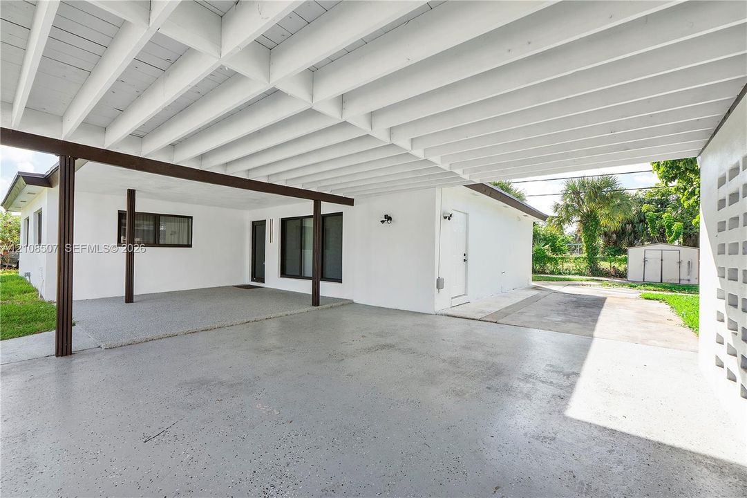 Covered carport featuring an exposed beam ceiling, smooth-finish concrete flooring, and a decorative concrete block privacy screen