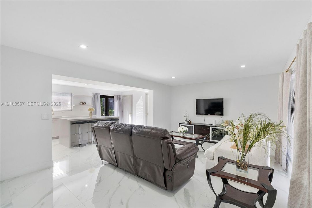 Large-format tile flooring, recessed ceiling lighting, and built-in kitchen peninsula with a stone-finish countertop