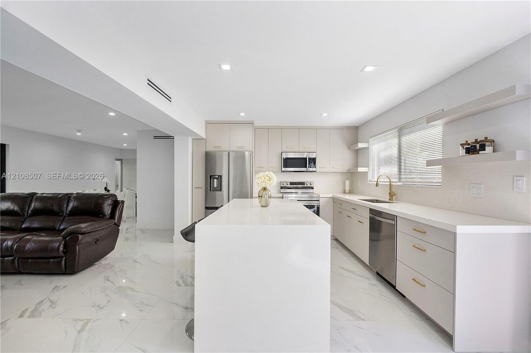 Kitchen featuring a stone-finish waterfall island, flat-panel cabinetry, stainless steel appliances, floating wall shelving, and large-format tile flooring
